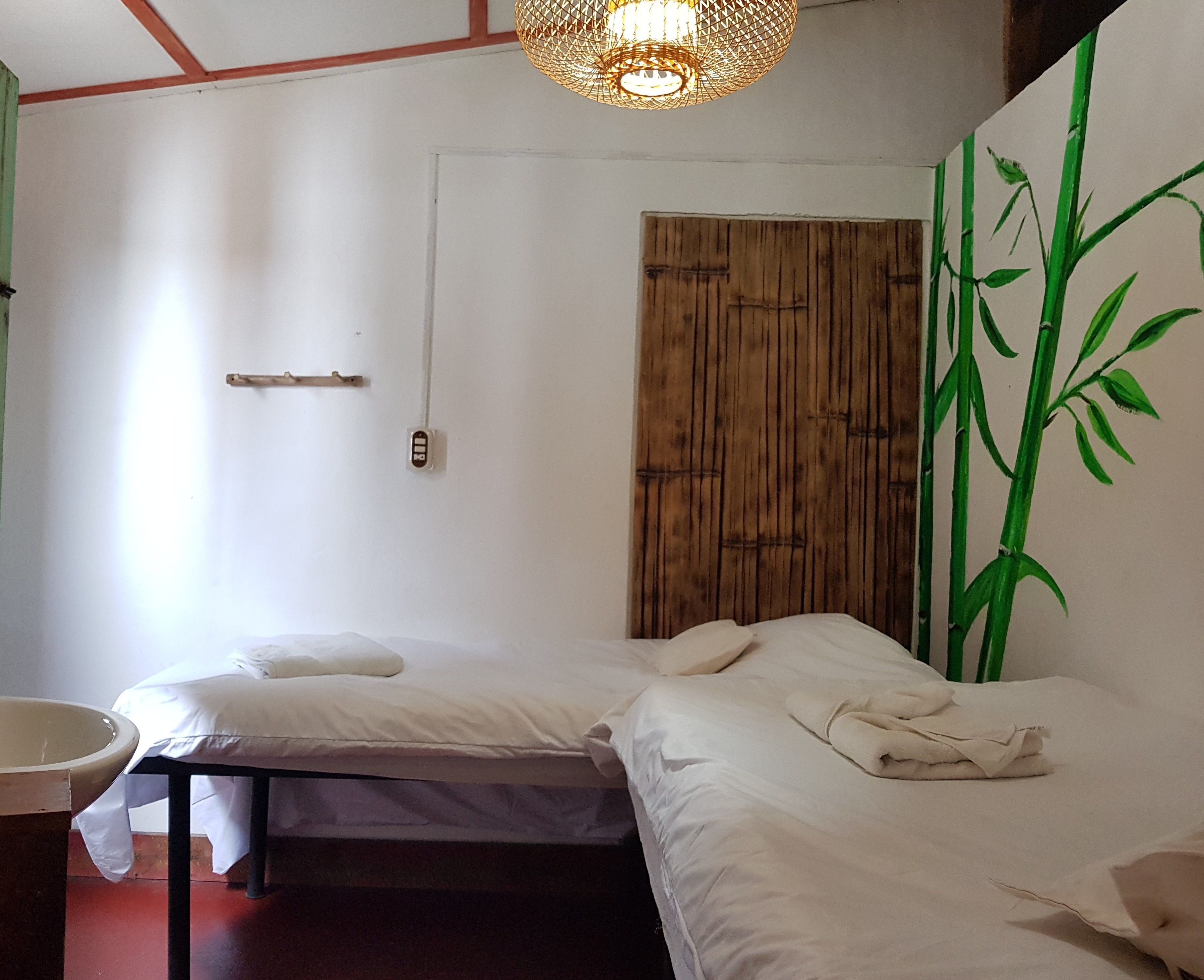 Una habitación con dos camas, una puerta de madera y un ventanal con una pintura de bambú.