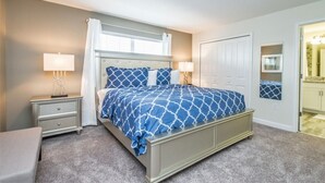 Un dormitorio con cama, mesitas de noche, ventana con cortinas, una puerta y un espejo.