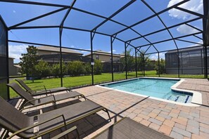 A covered outdoor swimming pool with lounge chairs, a brick patio, and a view of houses in the background. - Champions Gate-1430ATRGIL (Davenport)