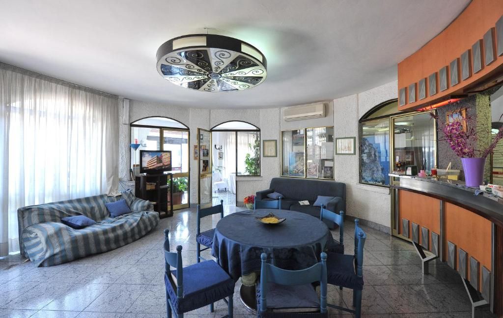 A modern living room with a sofa, round table, and chairs, a television, and a decorative ceiling light.