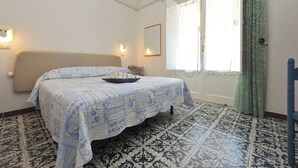Une chambre à coucher avec un lit, une table de chevet, un miroir et une fenêtre avec des rideaux.