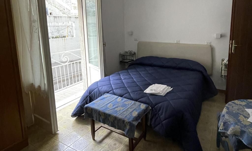Un dormitorio con cama, un banco, una mesita y una puerta que da a un balcón.