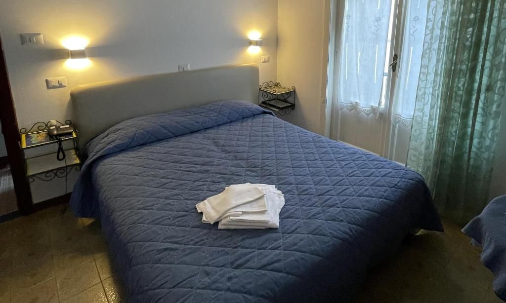 Una habitación de hotel con una cama, una mesita de noche con lámpara y una ventana con cortinas.