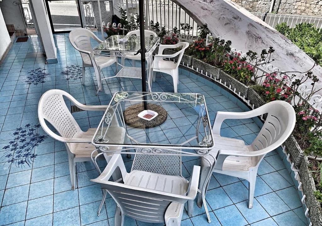 A patio with a round glass table surrounded by white plastic chairs, a tiled floor with blue floral patterns, and a white fence enclosing the area.