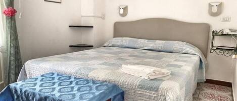 A bedroom with a bed, a bedside table, a wall-mounted shelf, and a picture on the wall.