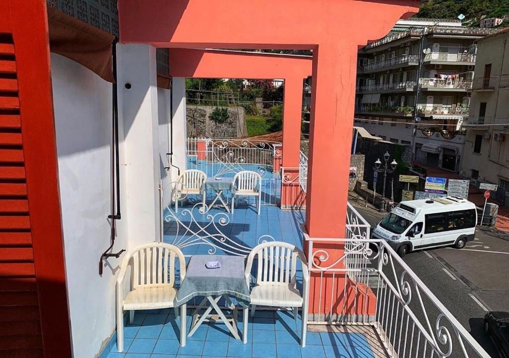 Varanda com cadeiras e mesas brancas, um toldo vermelho e vista para a rua com edifícios.