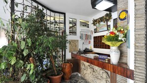 Un espace d’accueil comprenant un comptoir de réception, des plantes en pot, un tableau accroché au mur et un motif décoratif en forme de soleil.