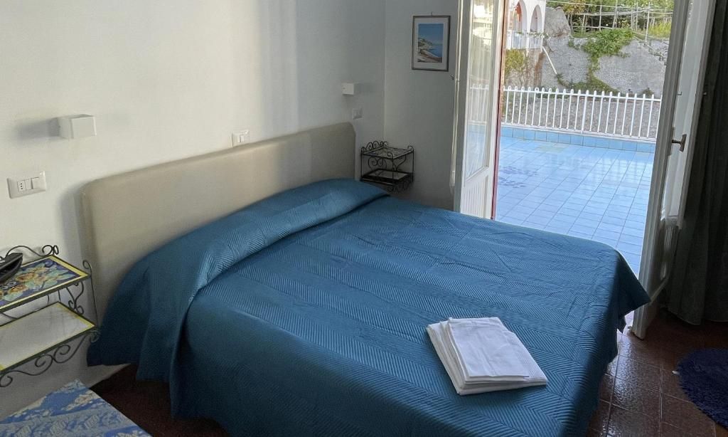 A bedroom with a bed, a small bedside table, a window with a view, and a door leading to an outdoor area.