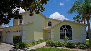 Uma casa de dois andares com fachada amarela, uma grande janela em arco e uma garagem frontal.