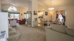 Uma sala de estar ampla com lareira, área de jantar com mesa e cadeiras, e cozinha ao fundo.