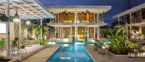 A modern two-story house with a swimming pool, outdoor seating, and lush greenery.