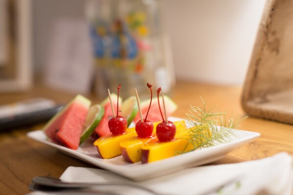 A plate of fruit skewers with watermelon and mango slices, garnished with dill and cherries, on a wooden table.