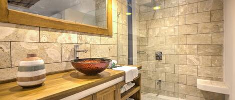 A bathroom with a wooden vanity, a large mirror, a bowl sink, and a shower area.