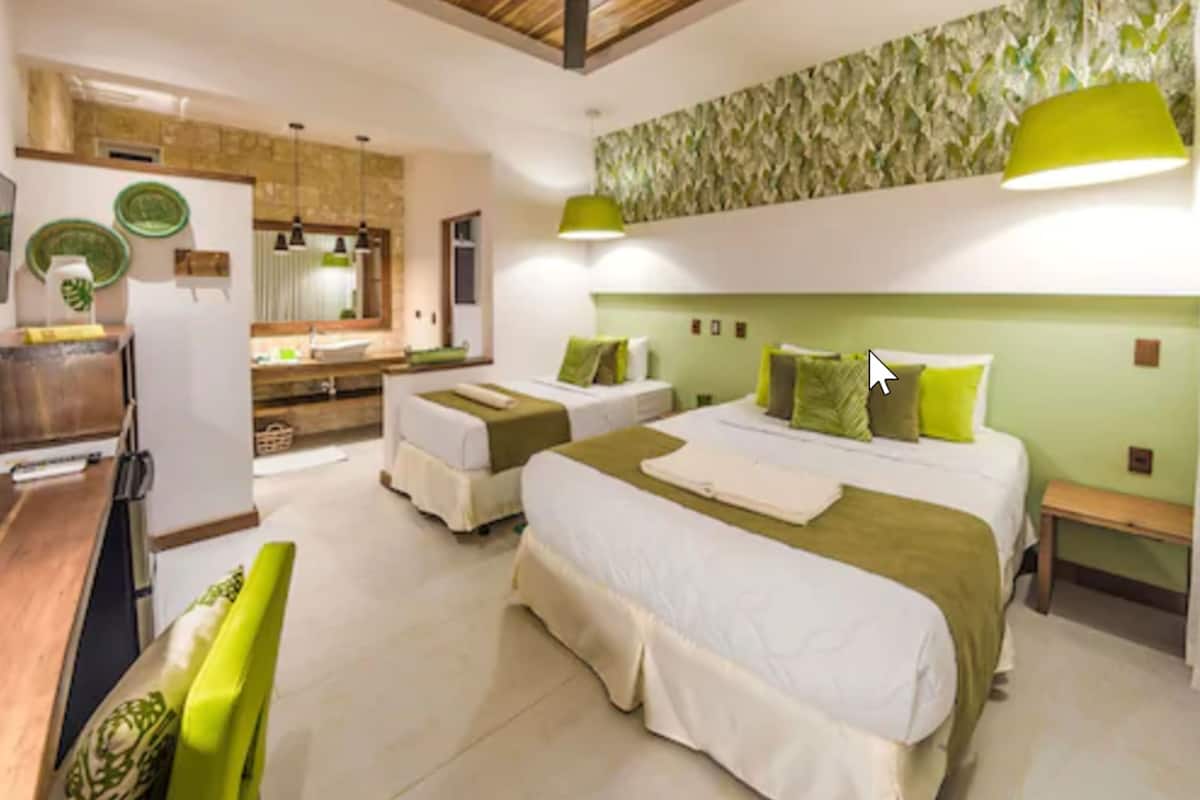 A hotel room with two beds, a kitchenette, and a bathroom.