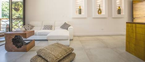 Una sala de estar moderna con un sofá blanco, cojines decorativos, una mesa de centro de madera y estanterías con jarrones.