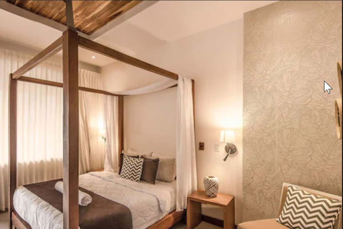A four-poster bed with a canopy, a bedside table with a lamp, and a patterned wall.