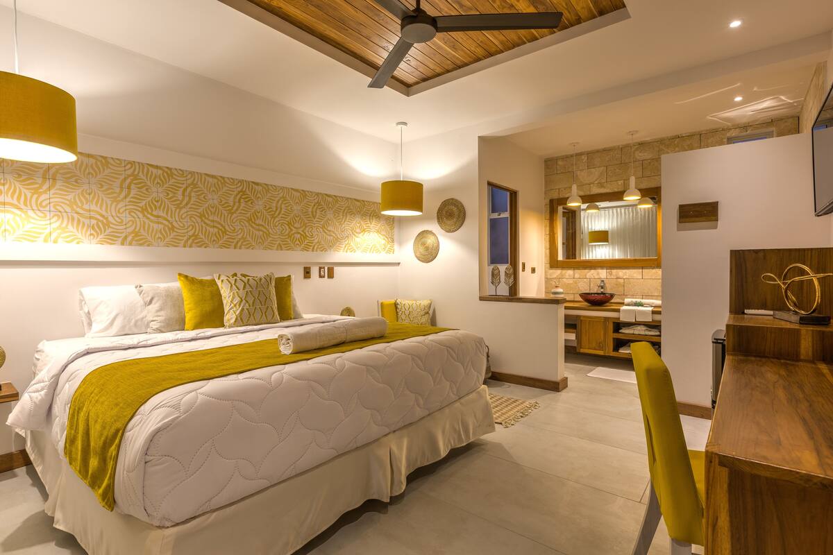 A modern bedroom with a large bed, a wooden ceiling, and a kitchen area with a sink and countertop.