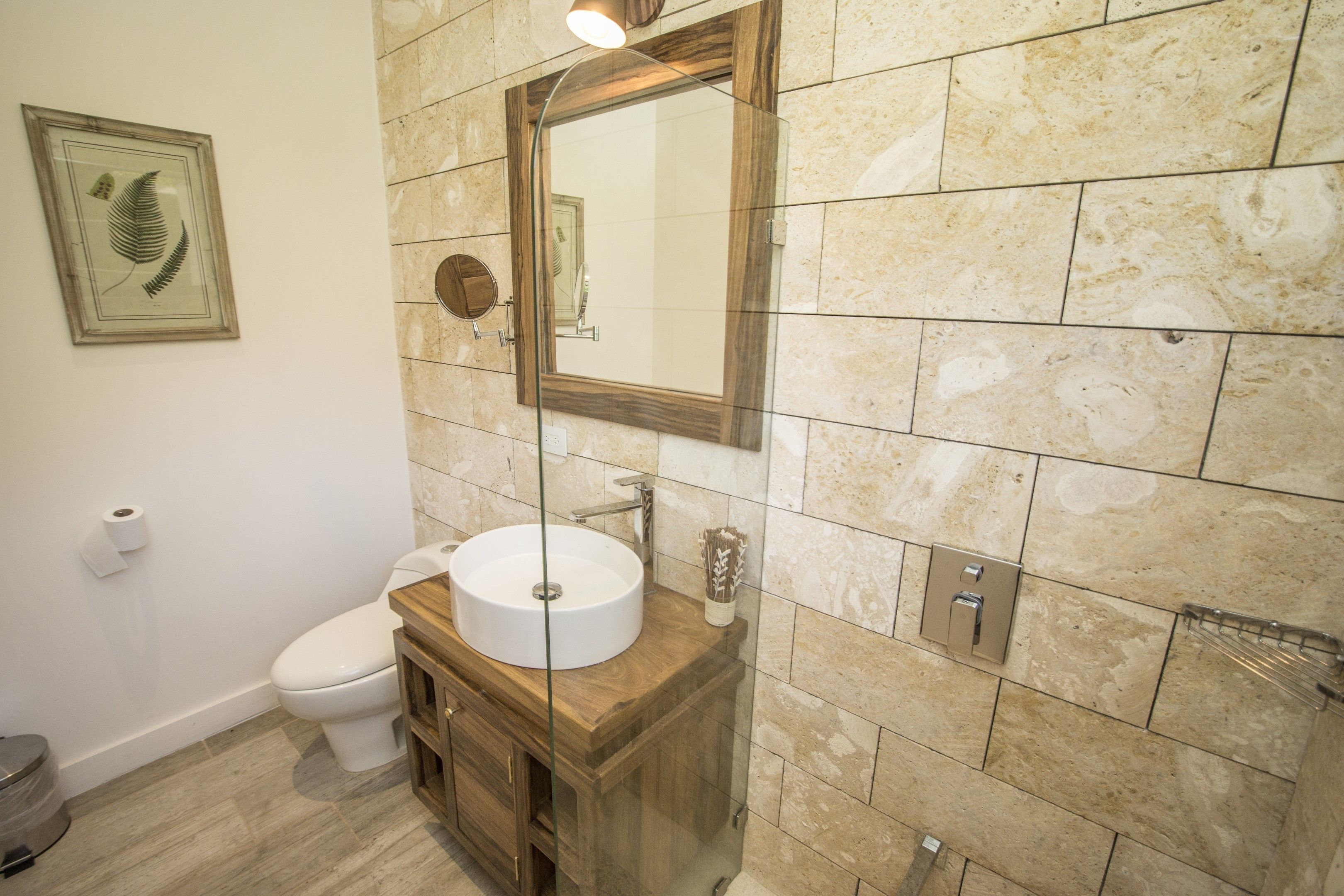 A bathroom with a wooden vanity, a round sink, a toilet, and a mirror with a wooden frame.