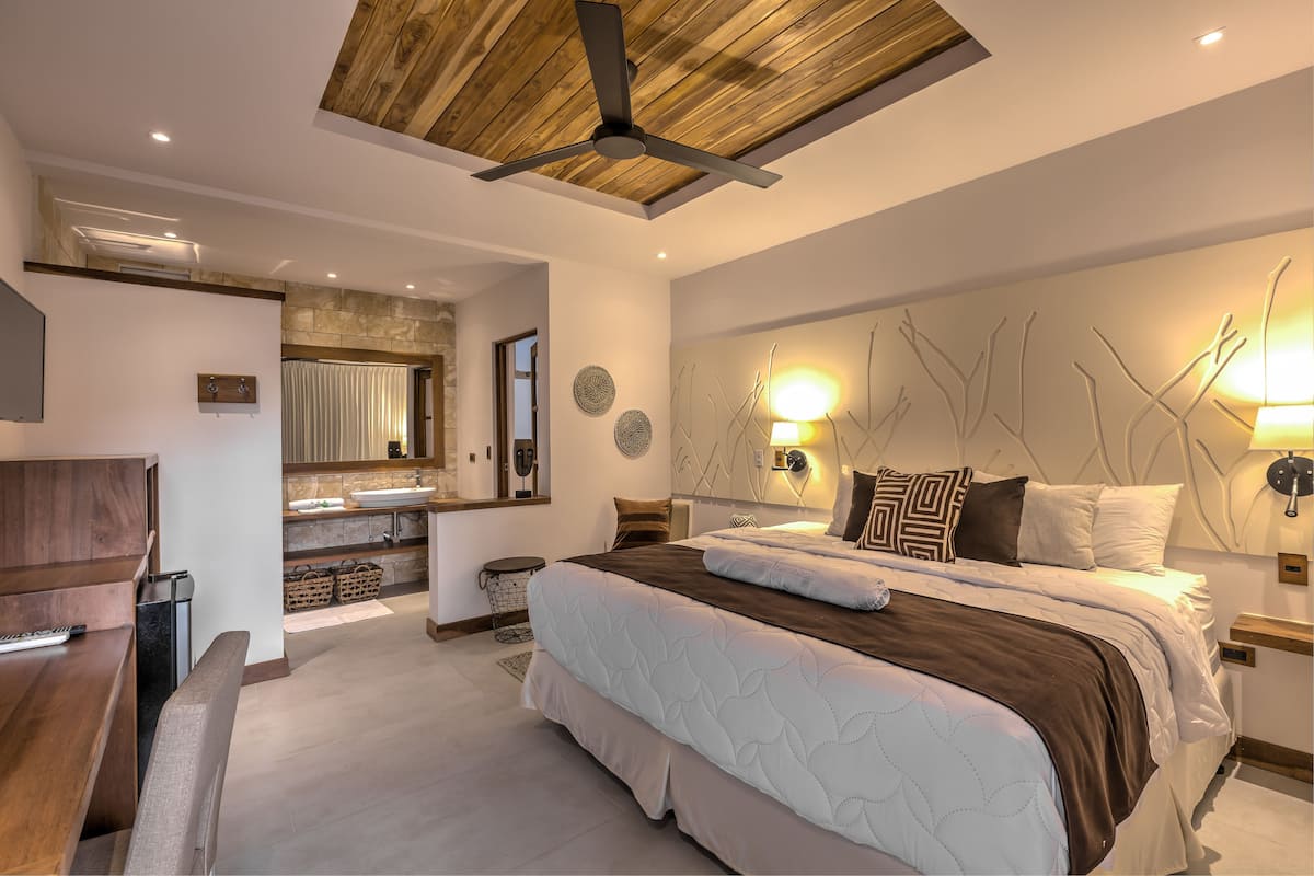 A modern bedroom with a large bed, a wooden ceiling, a built-in desk, and a bathroom with a stone wall.
