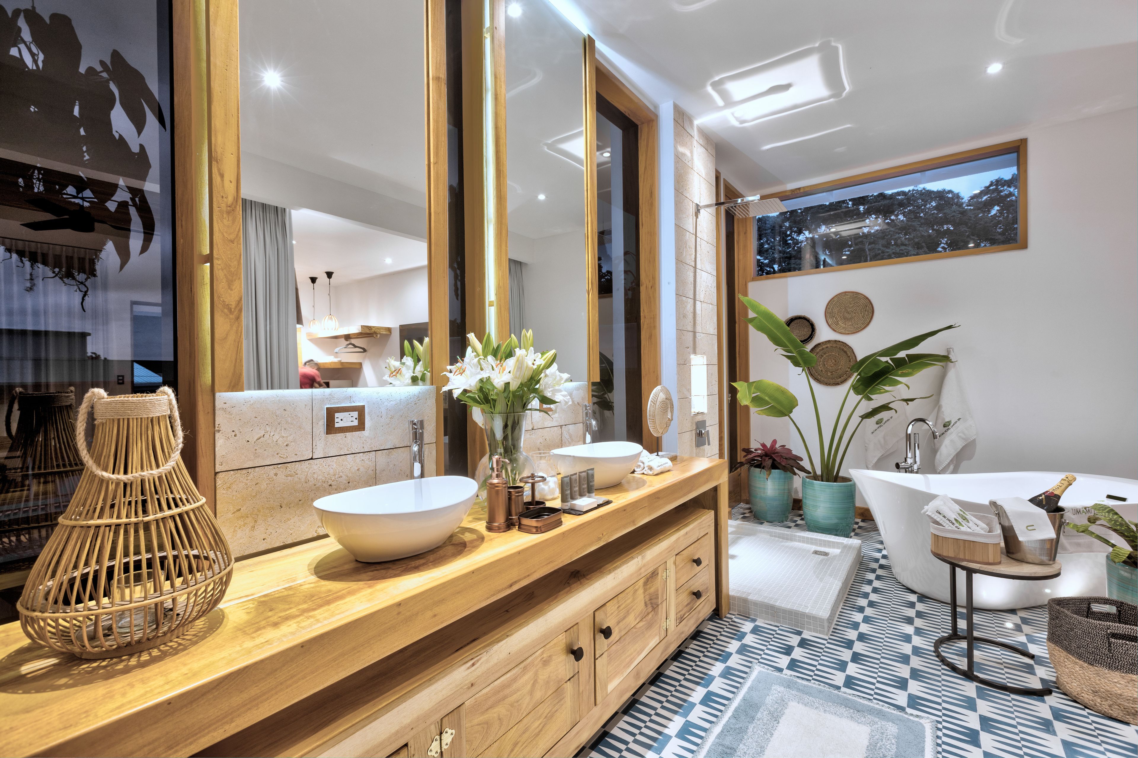 A modern bathroom with a wooden vanity, two sinks, a freestanding bathtub, and a large mirror.