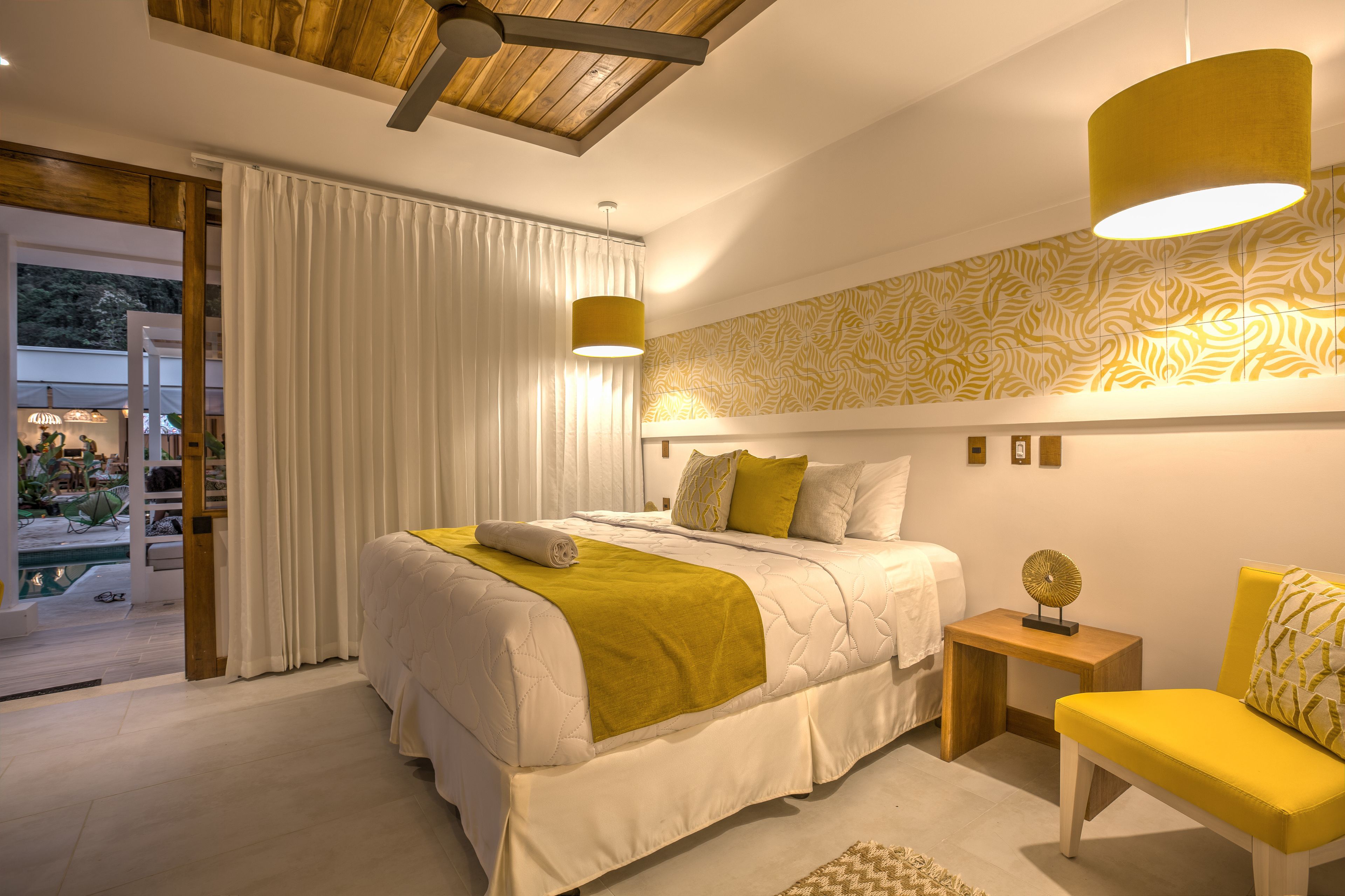 A modern bedroom with a large bed, a yellow armchair, and a small bedside table.