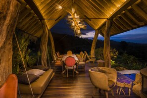 An outdoor dining area with a wooden deck, a central table, and chairs.