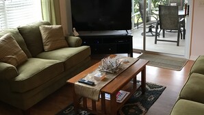 Een woonkamer met een bank, een salontafel, een televisie en een schuifdeur naar een terras.