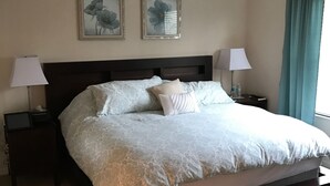 Een slaapkamer met een groot bed, twee nachtkastjes, twee wandlampen, een plafondventilator en twee florale kunstwerken in lijsten.