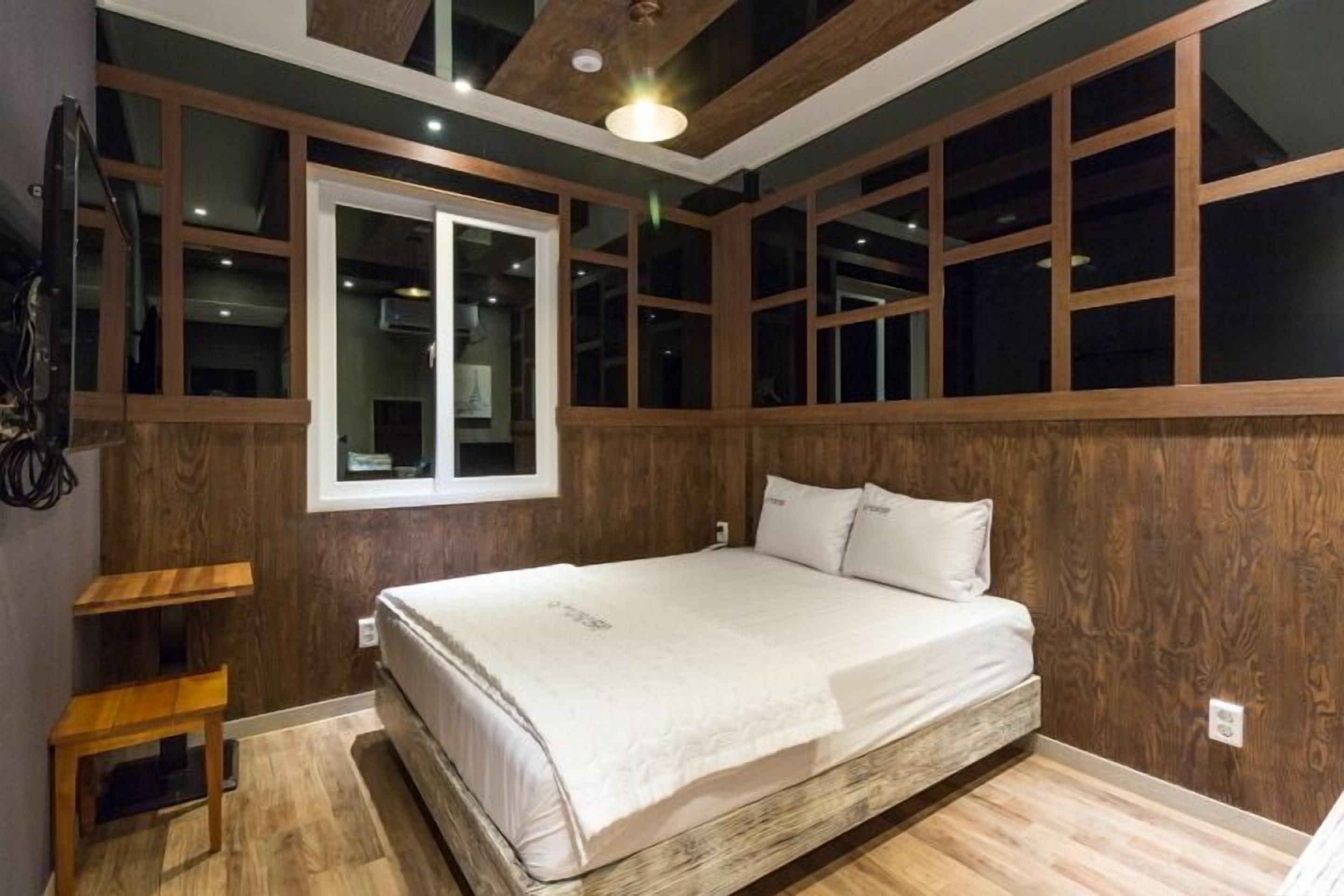 A bedroom with a bed, wooden paneling, a window, and a ceiling light.