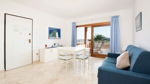 Ein modernes Wohnzimmer mit einem blauen Sofa, einem weißen Esstisch und einer Küchenzeile.