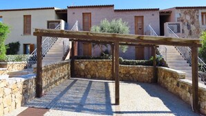 Ein Innenhof mit einer Holzpergola, Steinmauern und einer Treppe, die zu einem Gebäude mit Ziegeldach führt.