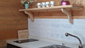 Een keuken met houten balken in het plafond, een wit aanrecht, een spoelbak en een plank met bekers en een waterkoker.