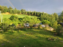 Un espacio verde con coches aparcados y árboles, cielo despejado y una montaña distante.