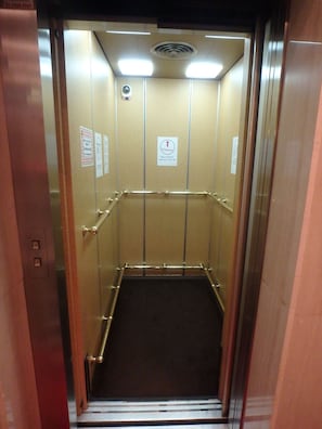 An elevator interior with metallic walls, a metal handrail, and a vent on the ceiling. - Hotel SUNTARGAS UENO (Tokyo)