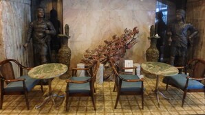 A dining area with marble walls, two statues, and four wooden chairs with blue cushions. - Hotel SUNTARGAS UENO (Tokyo)