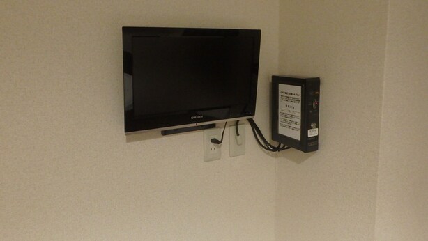 A flat-screen TV mounted on a wall with a power strip and a control panel beside it. - Hotel SUNTARGAS UENO (Tokyo)