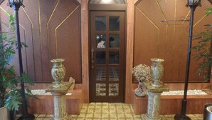 A wooden door with glass panels, flanked by two ornate street lamps and potted plants. - Hotel SUNTARGAS UENO (Tokyo)