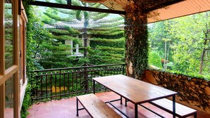 A balcony with a wooden bench, surrounded by lush greenery and a view of a garden. - Palazzo Pavone Gallery & Resort (Pak Chong)