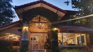 A restaurant with a covered entrance, outdoor seating, and a garden pathway. - Palazzo Pavone Gallery & Resort (Pak Chong)