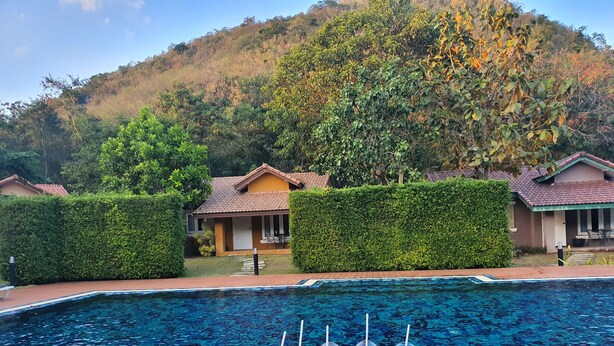 A poolside setting with a table of drinks and fruit, surrounded by a pool and houses in the background. - Palazzo Pavone Gallery & Resort (Pak Chong)