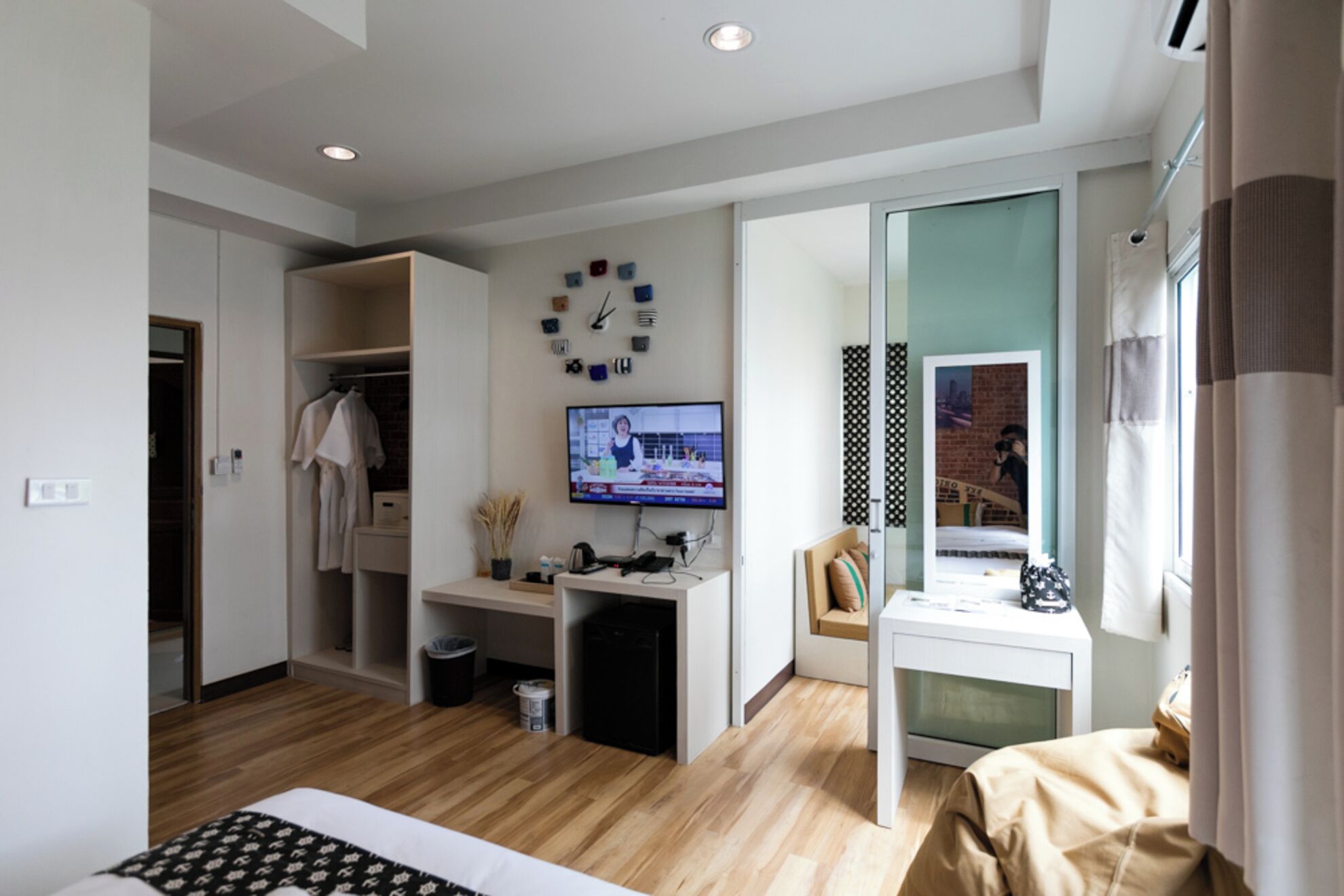 A modern bedroom with a wooden floor, a desk with a computer, a TV, and a bed.