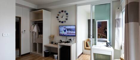 A modern bedroom with a wooden floor, a desk with a computer, a TV, and a bed.