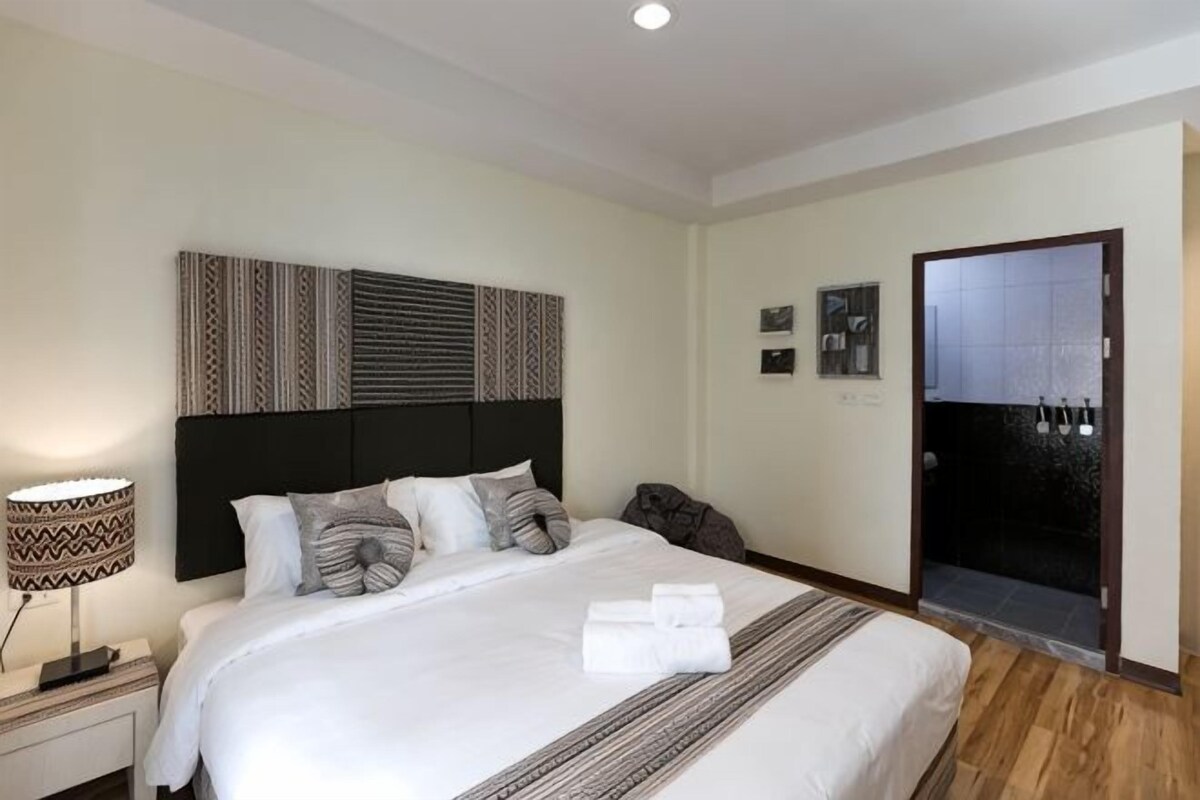 Ein Hotelzimmer mit einem großen Bett, einem Nachttisch mit Lampe, einem Bettkopfteil mit Muster und einer Tür zu einem Badezimmer.