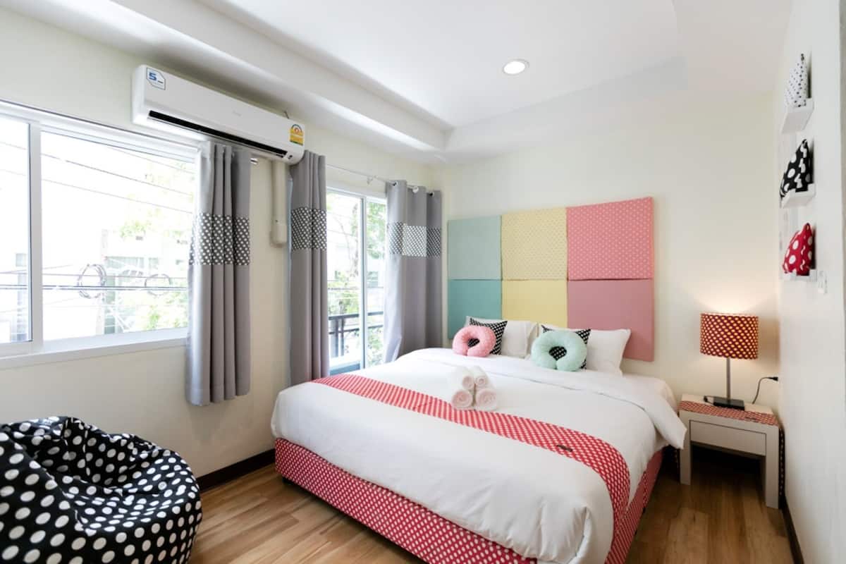 Une chambre à coucher moderne avec un grand lit, une table de chevet, une lampe et une fenêtre avec des rideaux.