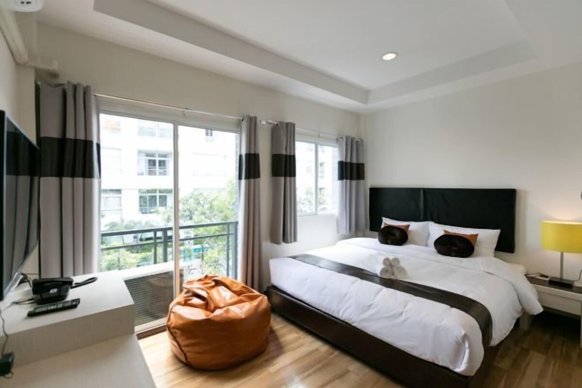 Ein modernes Hotelzimmer mit einem großen Bett, einem Schreibtisch mit Computer, einem Sitzsack und einem Balkon mit Vorhängen.