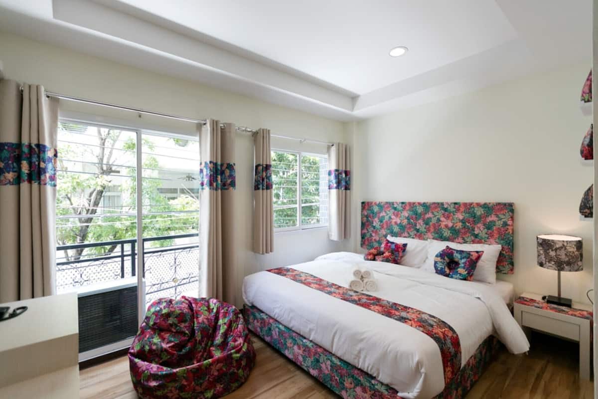 Une chambre à coucher avec un grand lit, une fenêtre avec des rideaux, une table de chevet et une chaise.