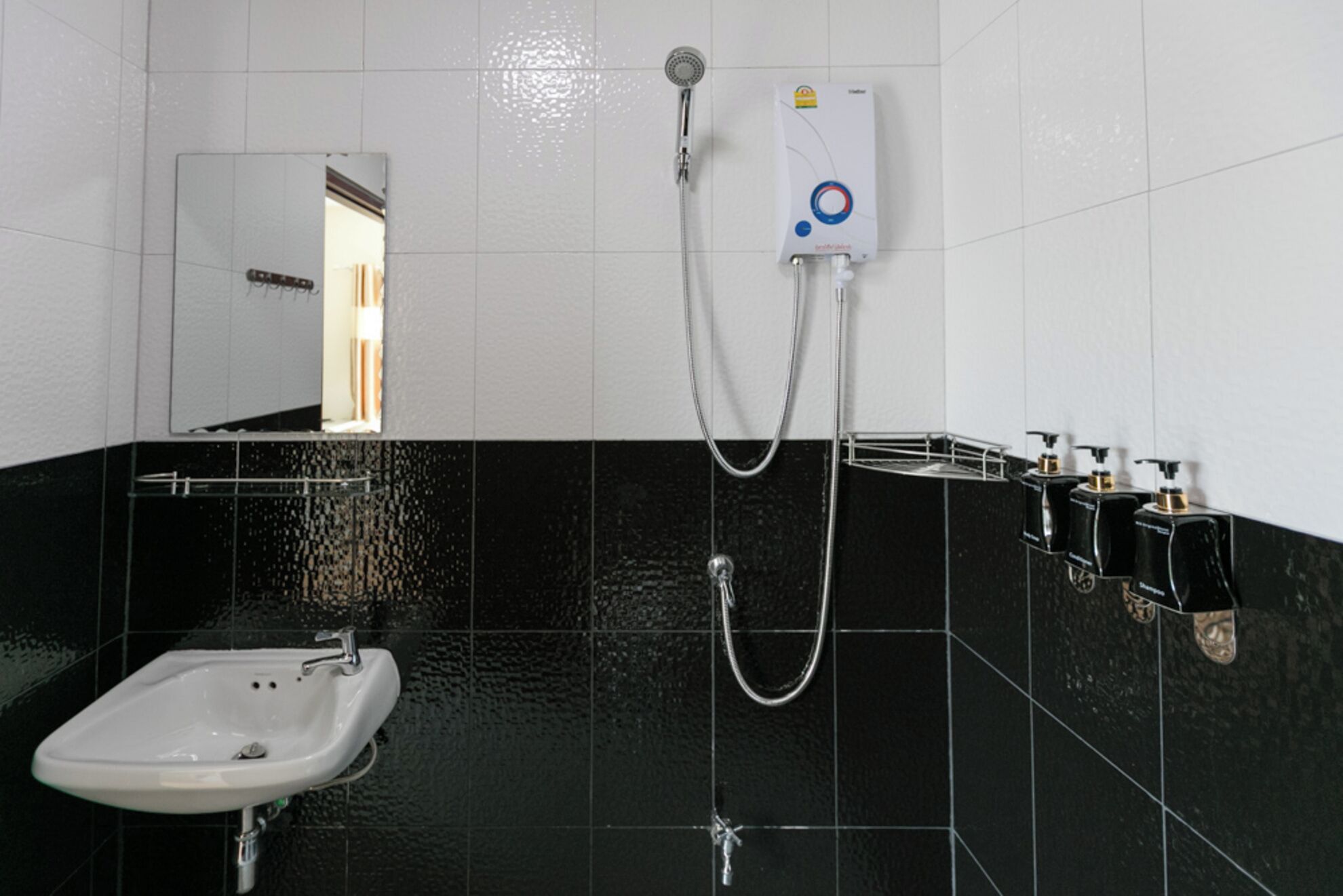 Uma casa de banho com lavatório branco, chuveiro com chuveiro manual e termoacumulador fixado na parede.