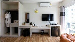 A modern hotel room with a wooden floor, a desk with a computer, a TV, a wardrobe, and a balcony with a view.