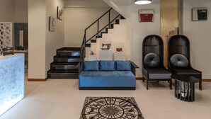 A modern living room with a blue sofa, a staircase, and a reception desk.