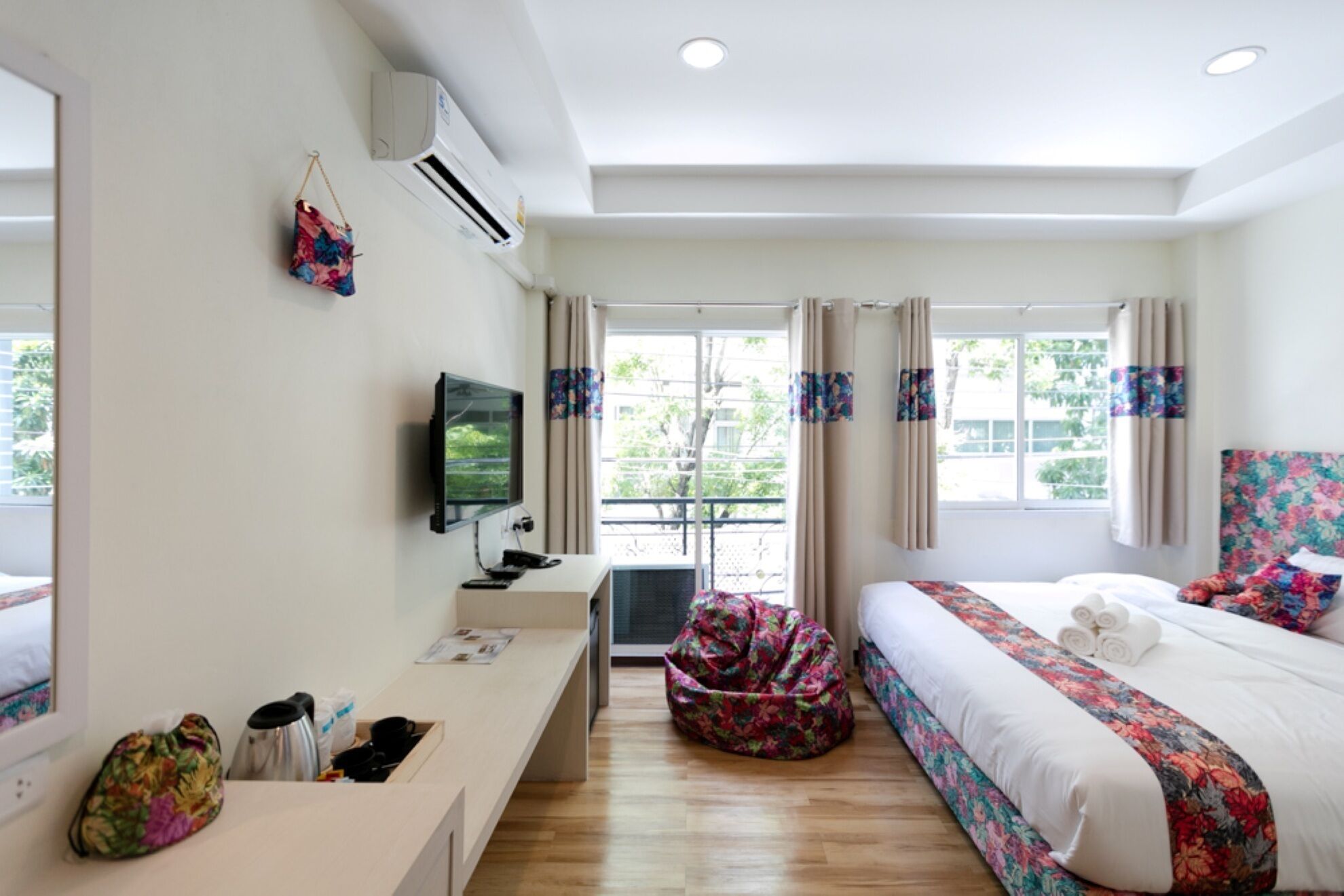 Ein Hotelzimmer mit einem Bett, einem Schreibtisch mit Computer, einer Klimaanlage und einem Fenster mit Vorhängen.